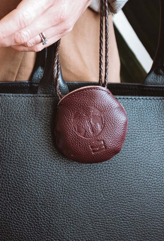 Journey Icon "Work" leather pouch with Congés Earth logo and office icon imprint, containing natural gemstones, is attached to a leather briefcase and carried by stylist woman professional.