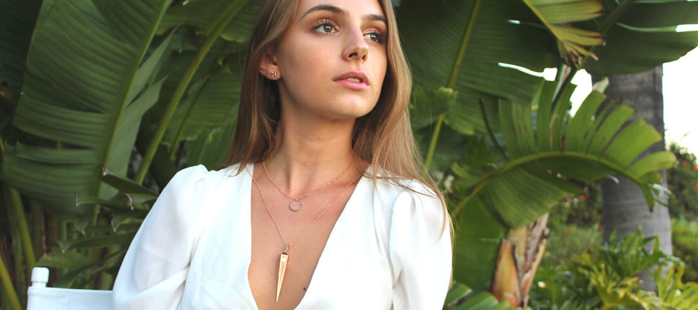 Model wears 14k solid reclaimed gold fine jewelry by sustainable jewelry brand Congés, created by a female entrepreneur. Gold pendulum necklace is layered with gold and diamond Scarab necklace, and gold stud earrings.