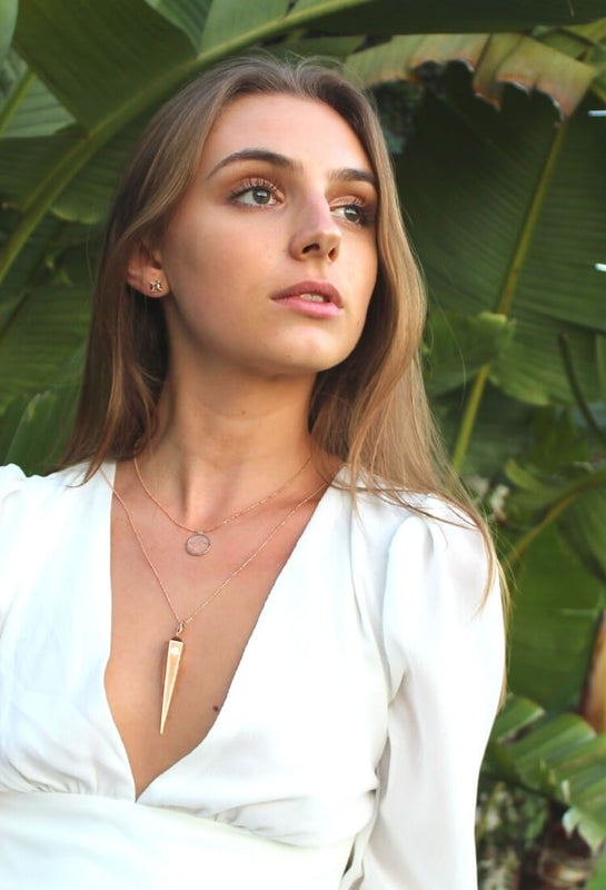 Model wears 14k solid reclaimed gold fine jewelry by sustainable jewelry brand Congés, created by a female entrepreneur. Gold pendulum necklace is layered with gold and diamond Scarab necklace, and gold stud earrings.
